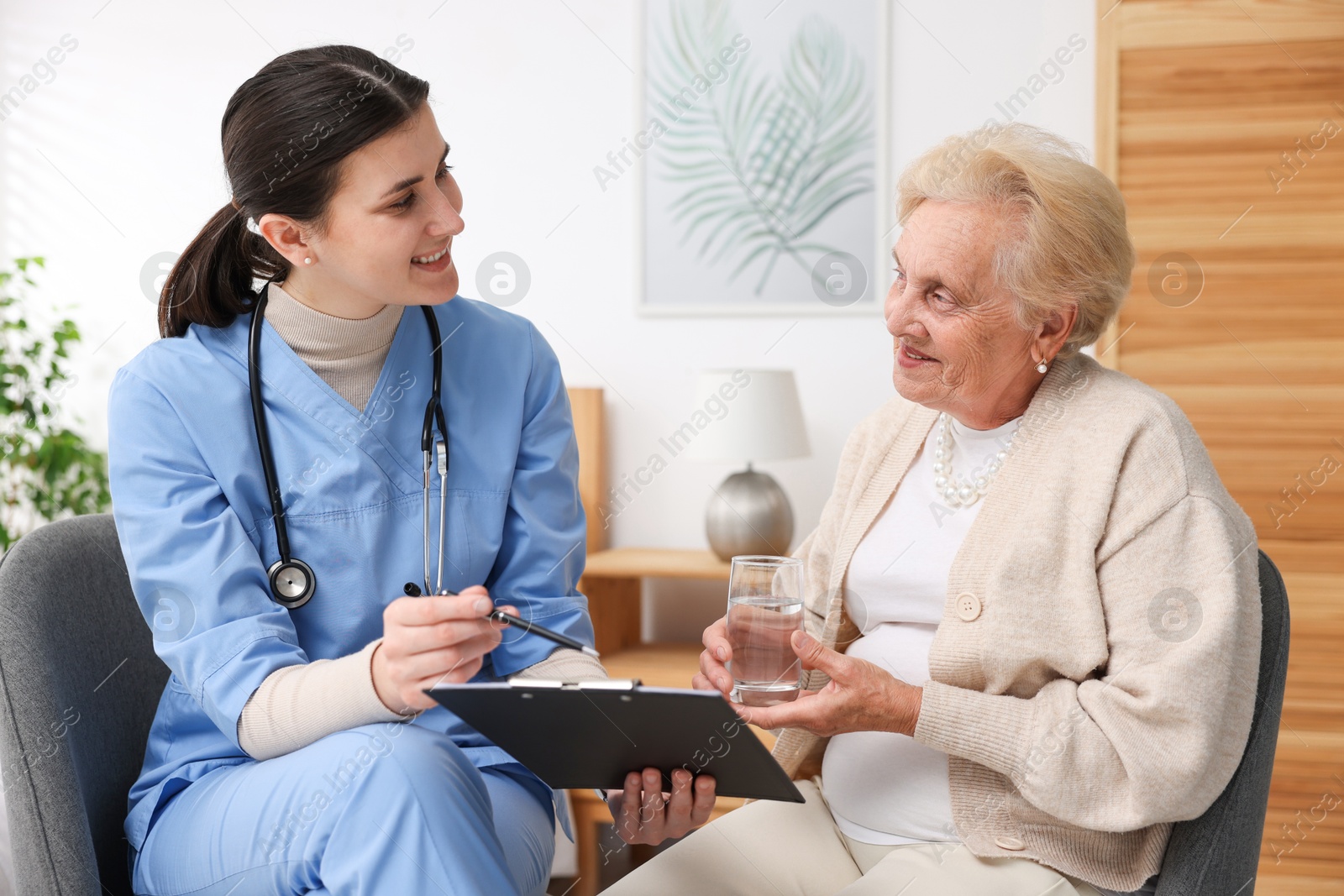 Nurse with clipboard examining senior woman indoors. Home health care service Photo of Nurse with clipboard examining senior woman indoors. Home health care service