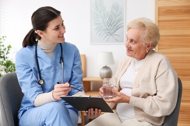 Photo of Nurse with clipboard examining senior woman indoors. Home health care service
