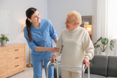 Photo of Nurse assisting senior woman with walking frame indoors. Home health care service