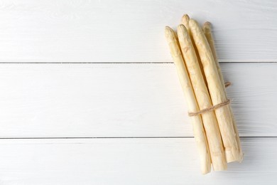 Photo of Bunch of raw asparagus spears on white wooden table, top view. Space for text