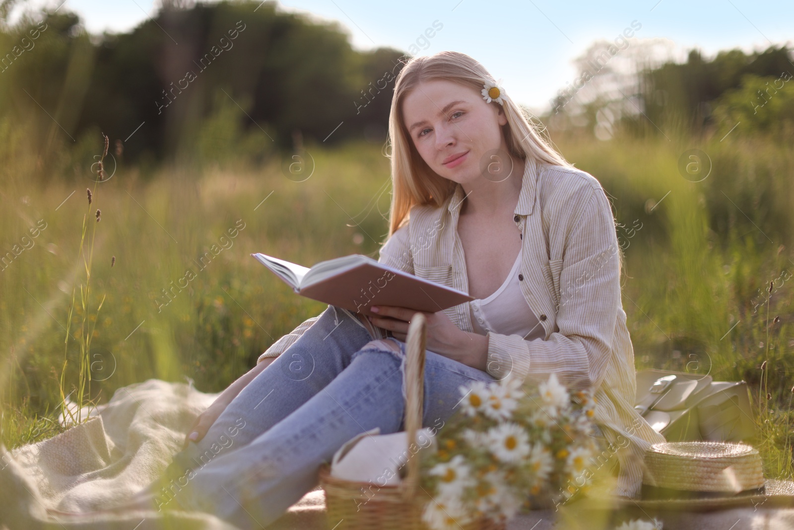 Beautiful woman with bouquet of wildflowers reading book on blanket in meadow Photo of Beautiful woman with bouquet of wildflowers reading book on blanket in meadow