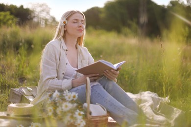 Photo of Beautiful woman with bouquet of wildflowers reading book on blanket in meadow