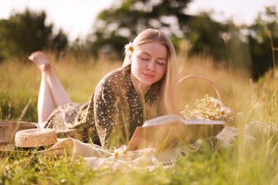 Photo of Beautiful woman with bouquet of wildflowers reading book on blanket in meadow