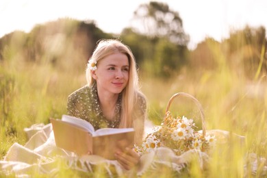Photo of Beautiful woman with bouquet of wildflowers reading book on blanket in meadow