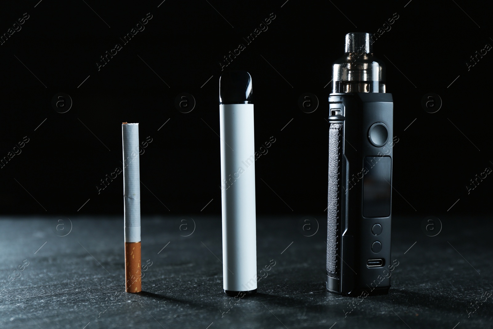 Electronic smoking devices and cigarettes on black table Photo of Electronic smoking devices and cigarettes on black table