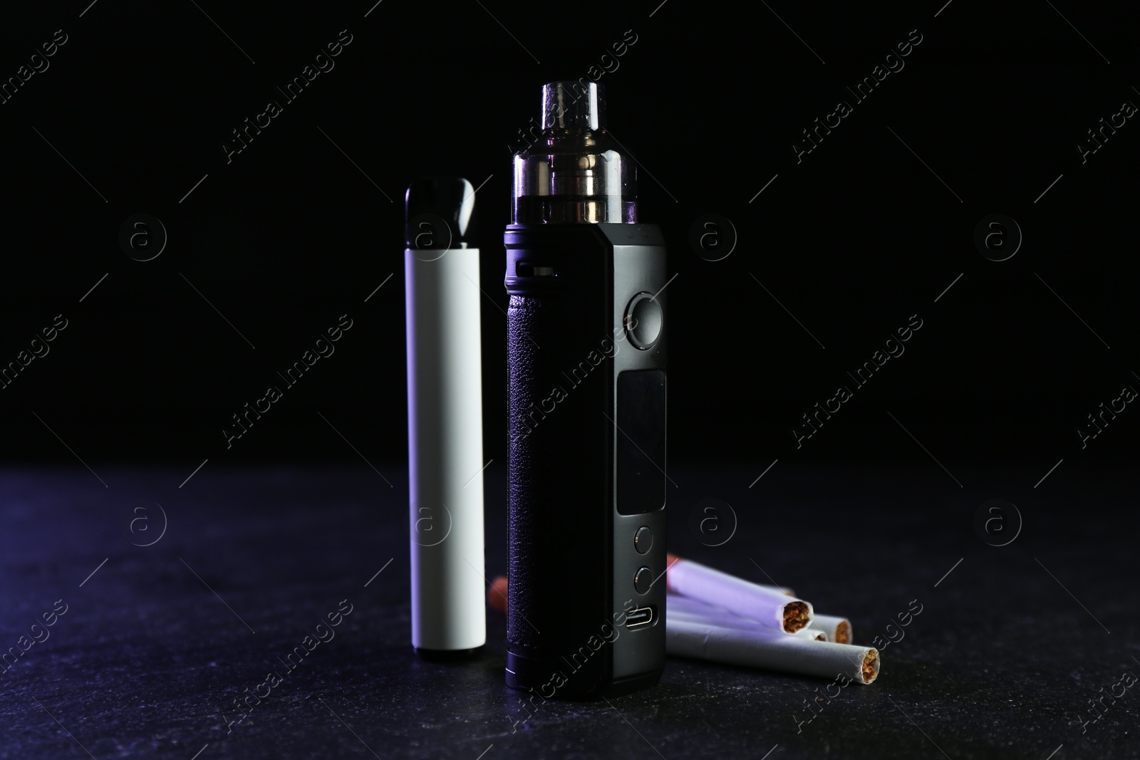 Electronic smoking devices and cigarettes on black table Photo of Electronic smoking devices and cigarettes on black table
