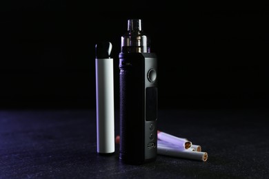 Photo of Electronic smoking devices and cigarettes on black table