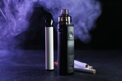 Photo of Electronic smoking devices and cigarettes on black table