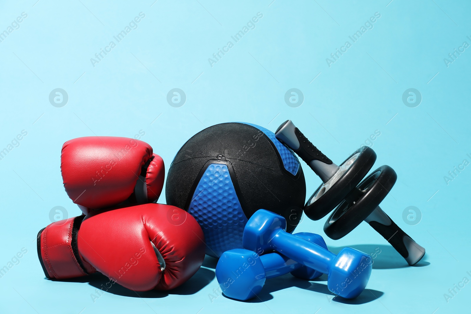 Medicine ball, boxing gloves, ab wheel and dumbbells on light blue background Photo of Medicine ball, boxing gloves, ab wheel and dumbbells on light blue background