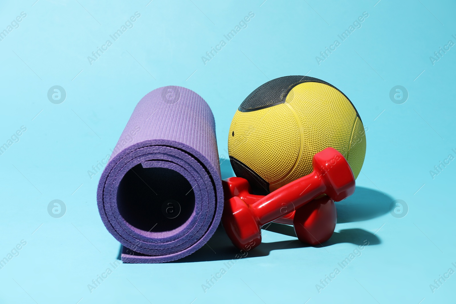 Photo of Medicine ball, fitness mat and dumbbells on light blue background