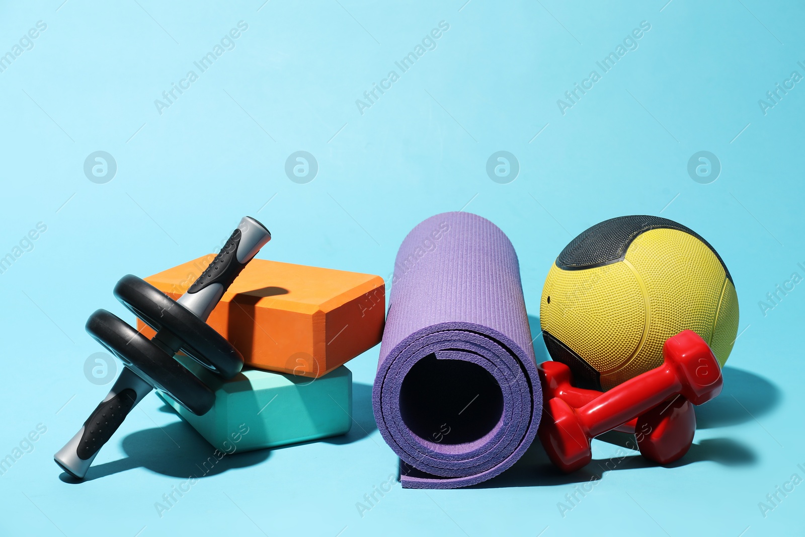 Photo of Medicine ball, ab wheel, foam blocks, fitness mat and dumbbells on light blue background