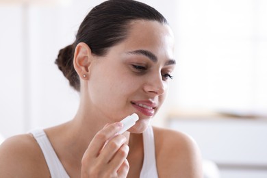 Photo of Young woman with lip balm at home
