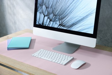 Photo of Stylish workplace with computer and pink mousepad on wooden table indoors, closeup