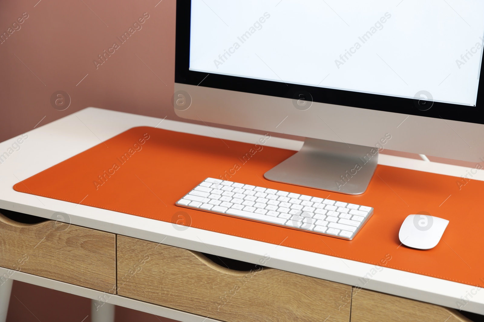 Photo of Stylish workplace with computer and orange mousepad on white table indoors, closeup