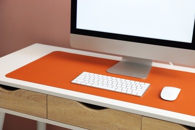 Photo of Stylish workplace with computer and orange mousepad on white table indoors, closeup