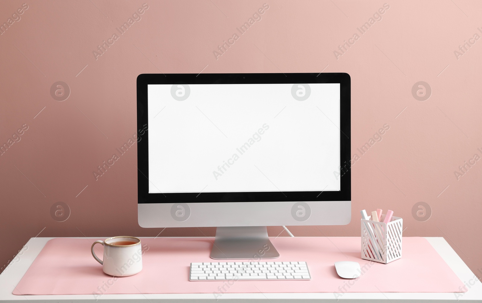 Photo of Stylish workplace with computer and pink mousepad on white table indoors. Space for text