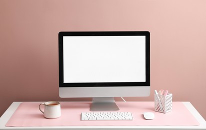 Photo of Stylish workplace with computer and pink mousepad on white table indoors. Space for text