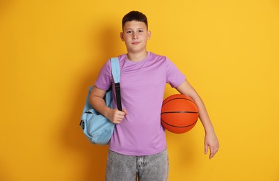 Photo of Teenage boy with backpack and basketball ball on orange background
