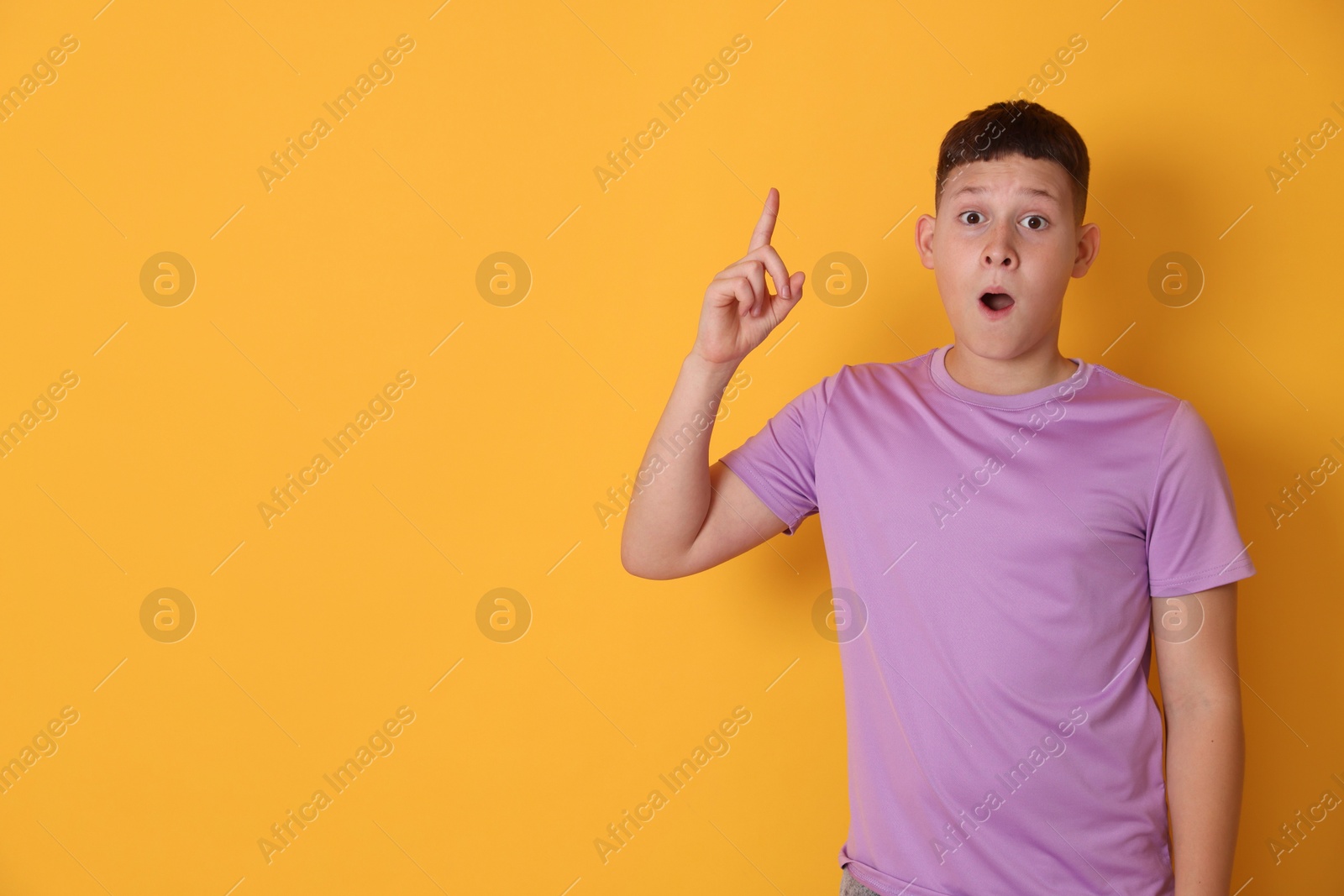 Photo of Teenage boy pointing at something on orange background, space for text