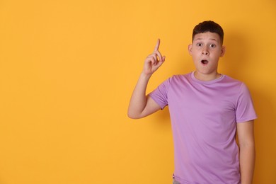 Photo of Teenage boy pointing at something on orange background, space for text