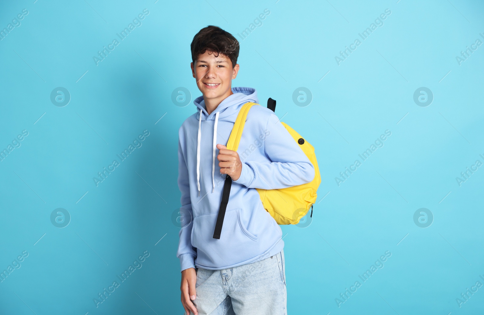 Teenage boy with backpack on light blue background Photo of Teenage boy with backpack on light blue background