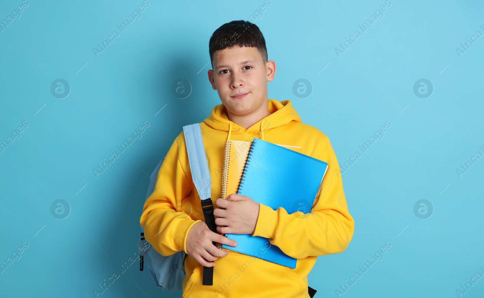 Teenage boy with backpack and notebooks on light blue background Photo of Teenage boy with backpack and notebooks on light blue background