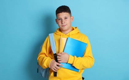 Photo of Teenage boy with backpack and notebooks on light blue background