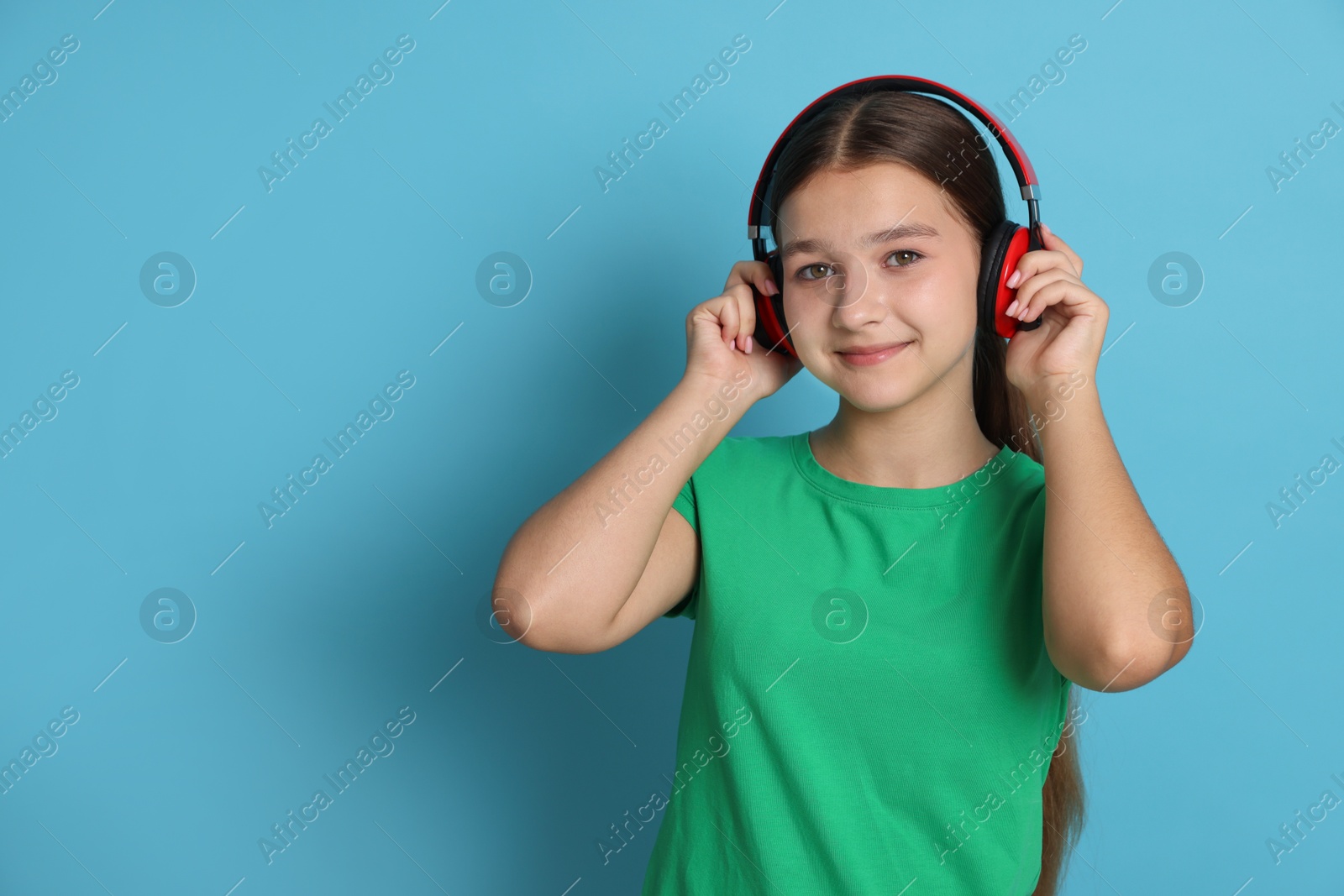 Photo of Teenage girl in headphones on light blue background, space for text