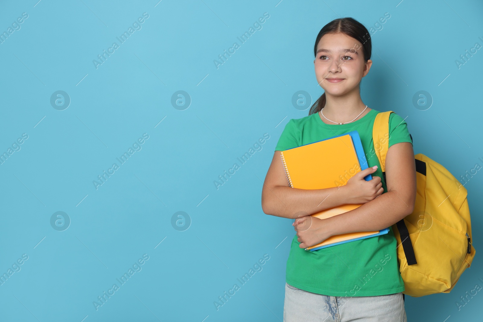 Teenage girl with backpack and notebooks on light blue background, space for text Photo of Teenage girl with backpack and notebooks on light blue background, space for text