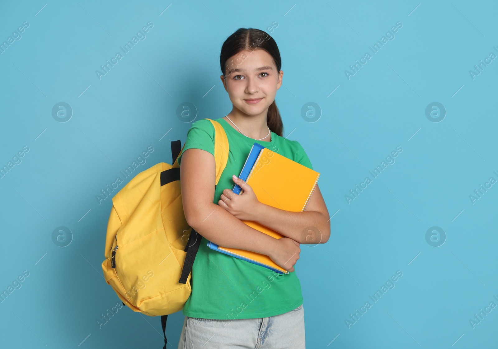 Teenage girl with backpack and notebooks on light blue background Photo of Teenage girl with backpack and notebooks on light blue background