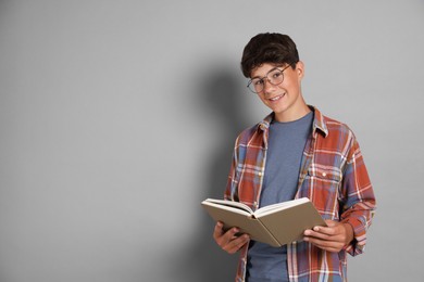 Photo of Teenage boy reading book on grey background, space for text
