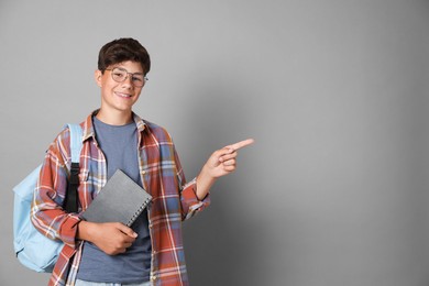 Photo of Teenage boy with notebook and backpack pointing at something on grey background, space for text