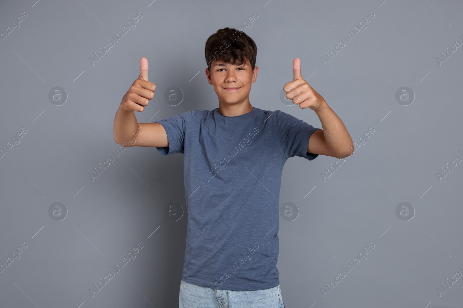 Teenage boy showing thumbs up on grey background Photo of Teenage boy showing thumbs up on grey background