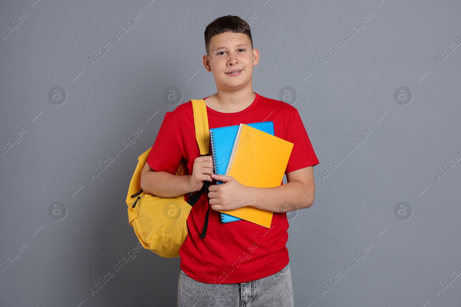 Teenage boy with notebooks and backpack on grey background Photo of Teenage boy with notebooks and backpack on grey background