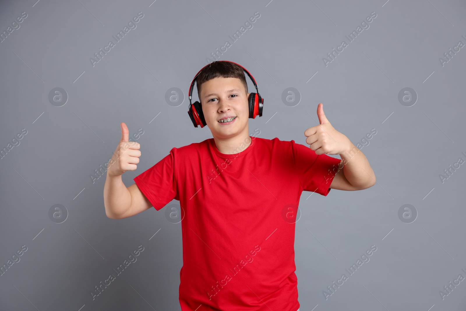 Teenage boy in headphones showing thumbs up on grey background Photo of Teenage boy in headphones showing thumbs up on grey background