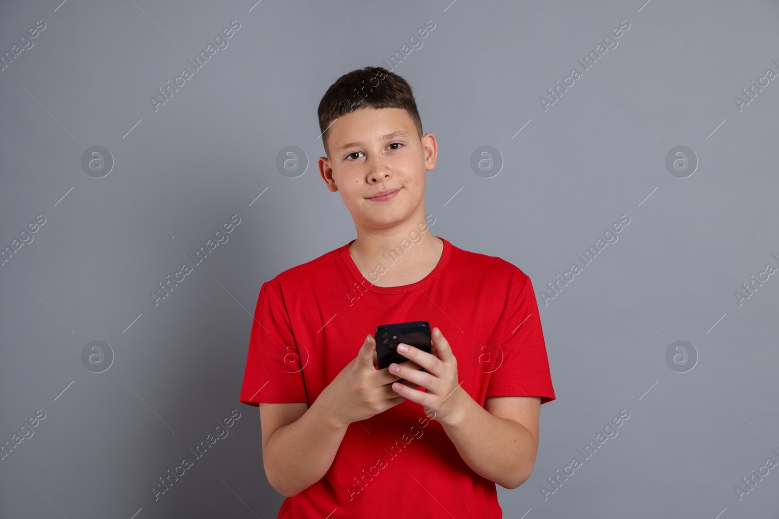 Teenage boy with smartphone on grey background Photo of Teenage boy with smartphone on grey background