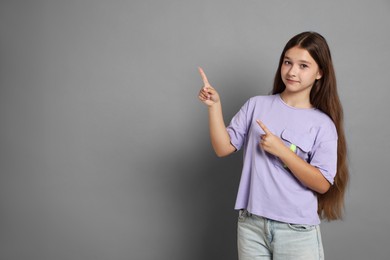 Photo of Teenage girl pointing at something on grey background, space for text
