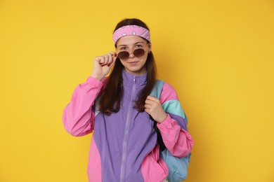 Photo of Teenage girl in sunglasses with backpack on yellow background