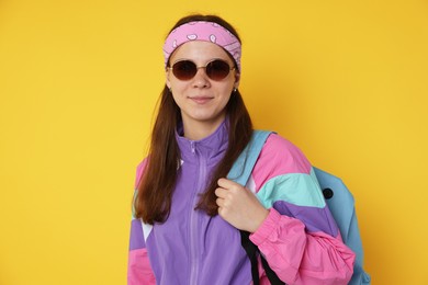 Photo of Teenage girl in sunglasses with backpack on yellow background