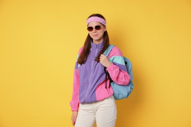 Photo of Teenage girl in sunglasses with backpack on yellow background