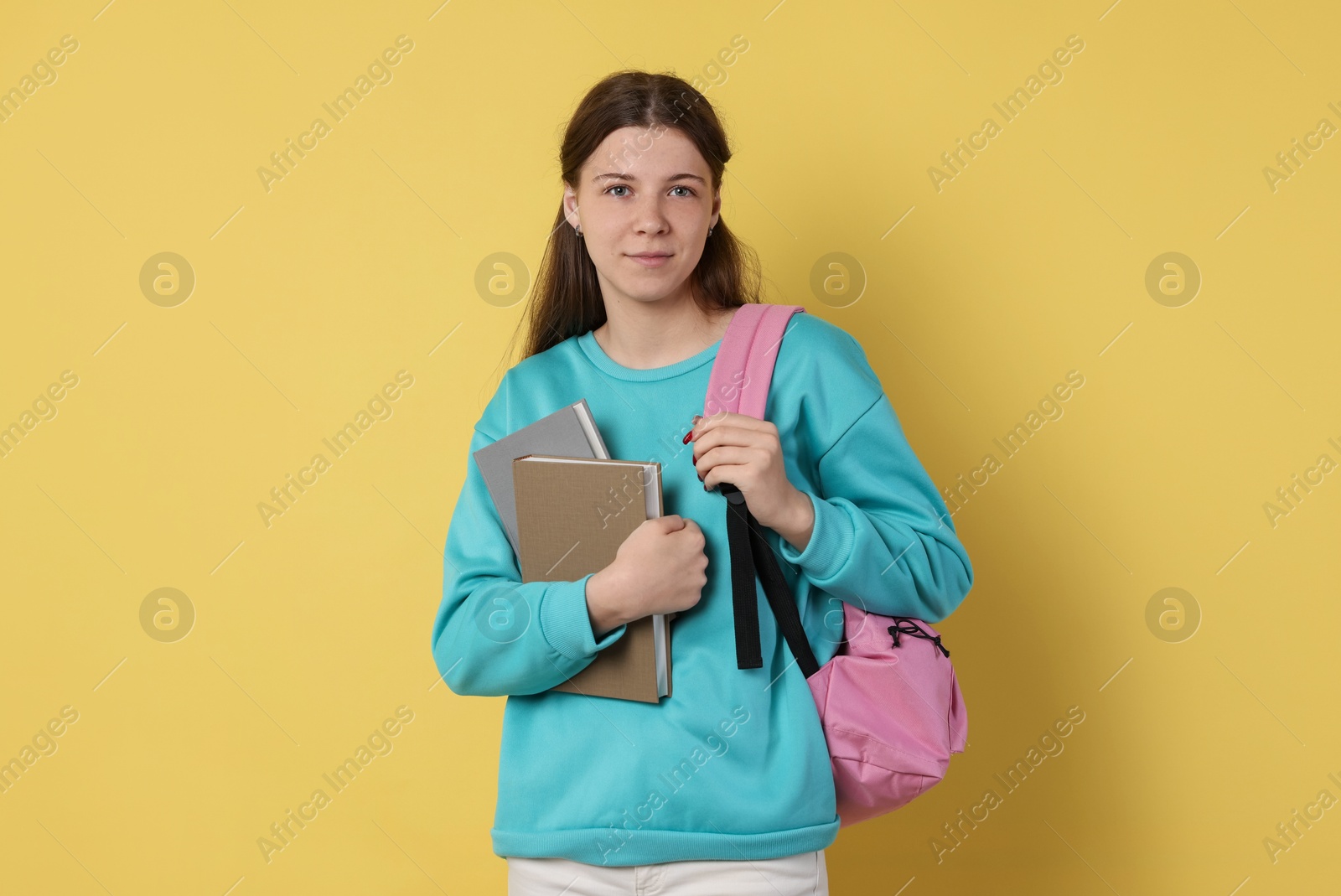 Teenage girl with backpack and books on yellow background Photo of Teenage girl with backpack and books on yellow background