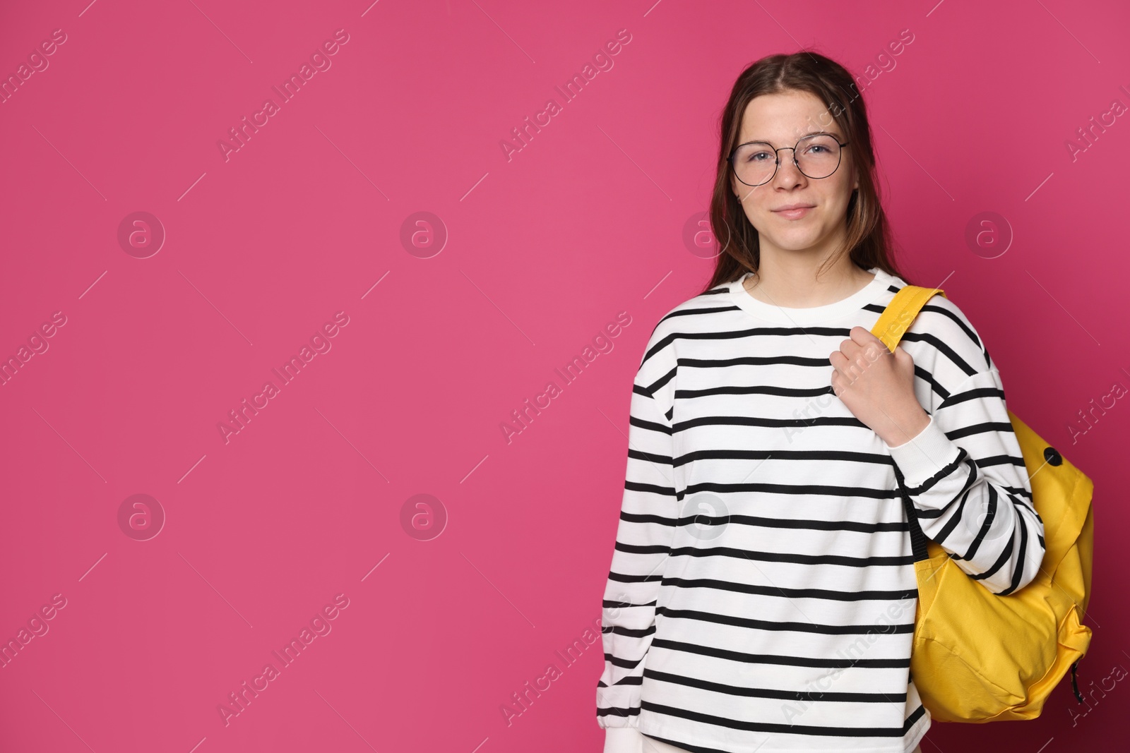 Teenage girl in glasses with backpack on crimson background, space for text Photo of Teenage girl in glasses with backpack on crimson background, space for text