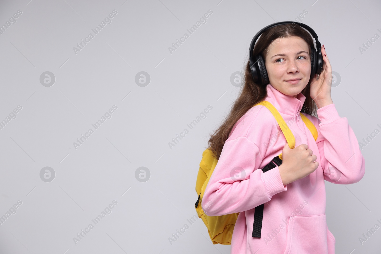 Teenage girl in headphones with backpack on light grey background, space for text Photo of Teenage girl in headphones with backpack on light grey background, space for text