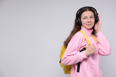 Photo of Teenage girl in headphones with backpack on light grey background, space for text