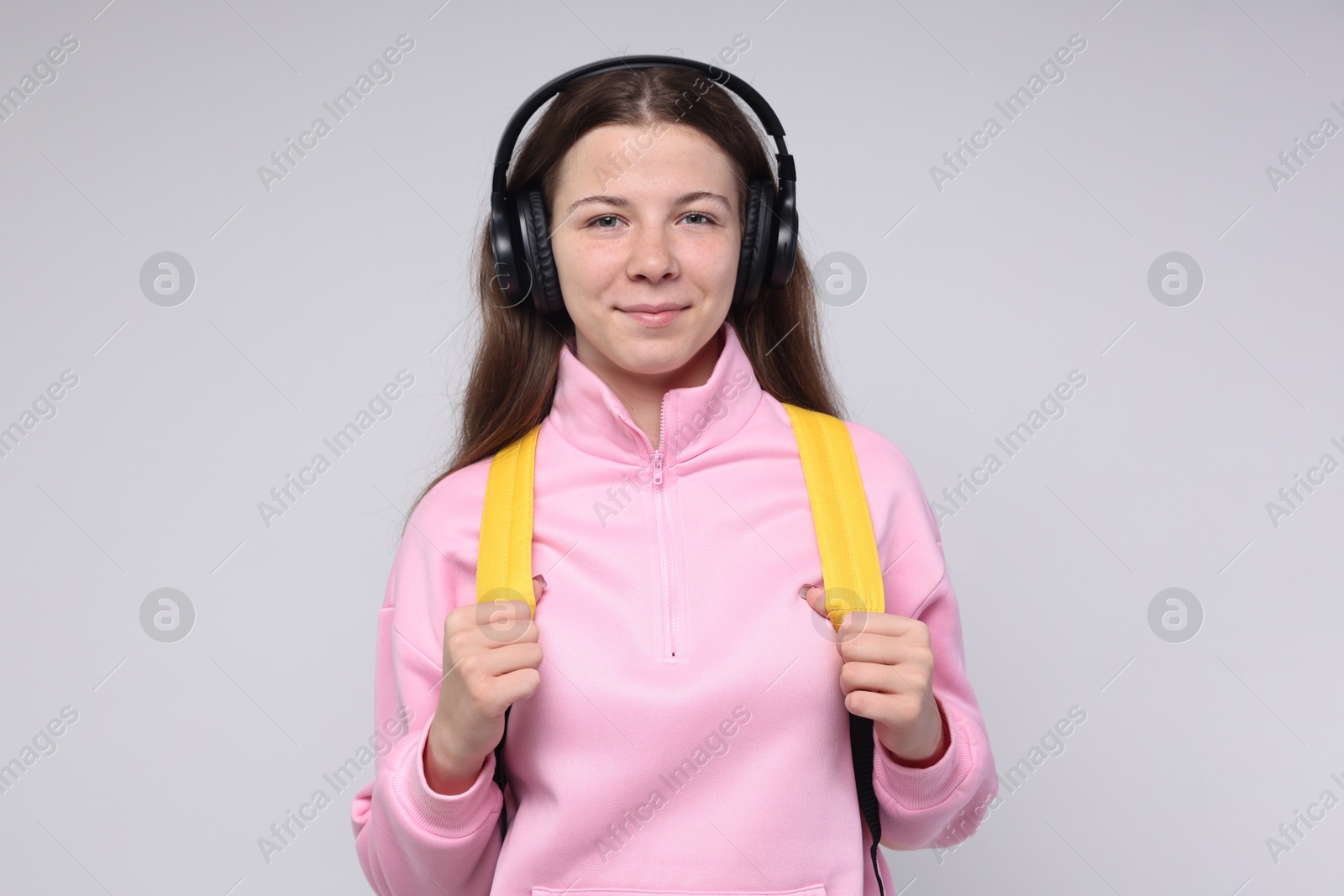 Teenage girl in headphones with backpack on light grey background, space for text Photo of Teenage girl in headphones with backpack on light grey background, space for text