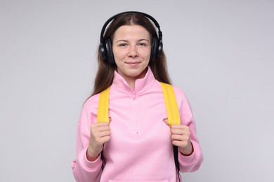 Photo of Teenage girl in headphones with backpack on light grey background, space for text