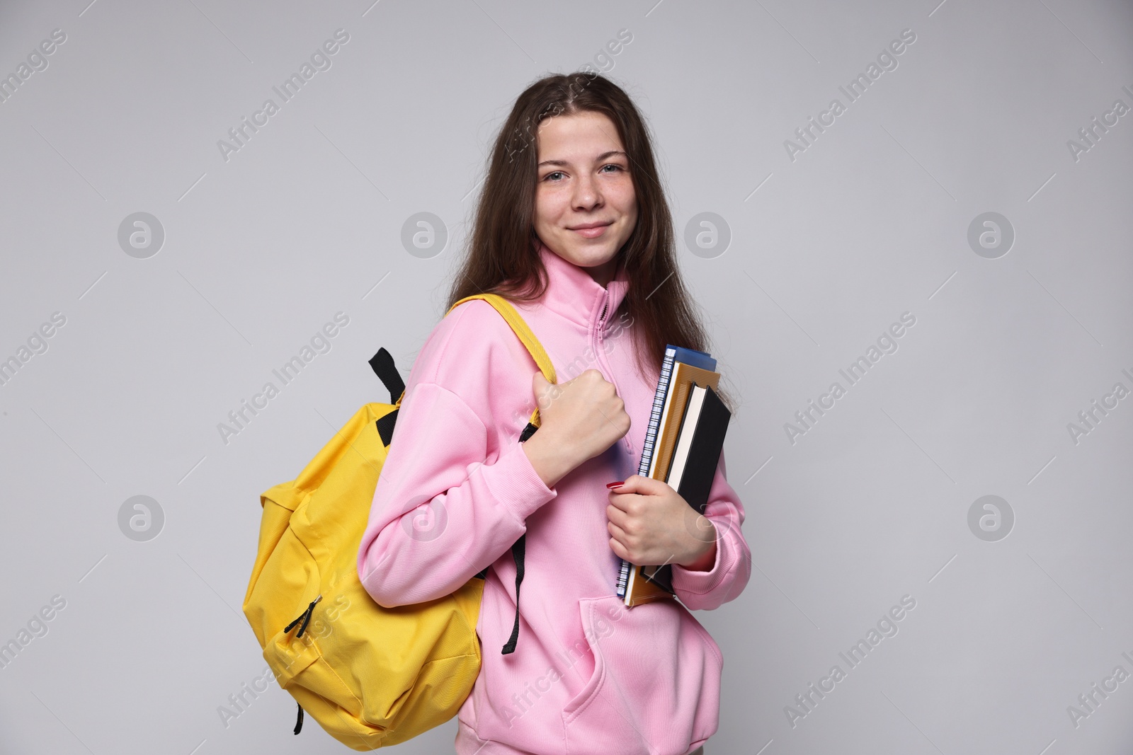 Teenage girl with backpack and notebooks on light grey background Photo of Teenage girl with backpack and notebooks on light grey background