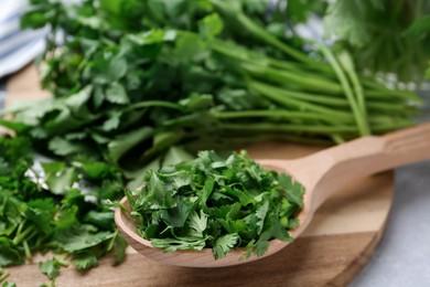 Photo of Fresh green cilantro and wooden spoon on table, closeup