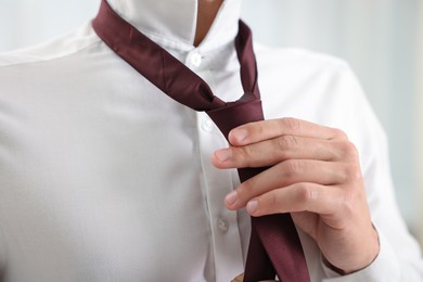 Photo of Man tying stylish necktie at home, closeup