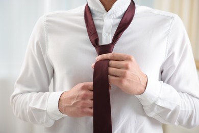 Photo of Man tying stylish necktie at home, closeup